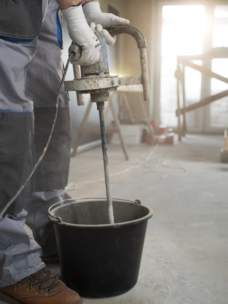 zdjęcie przedstawia osobę mieszającą wylewkę w wiadrze